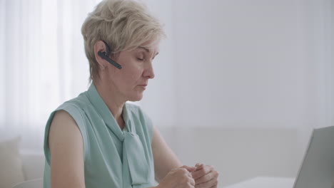 La-Anciana-Se-Comunica-En-Línea-Mediante-Videollamada-Usando-Auriculares-Y-Portátiles,-Consulta-En-Línea-Y-Trabajo-A-Distancia